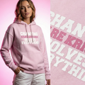 Person wearing a pink hoodie with text, standing against a pink background