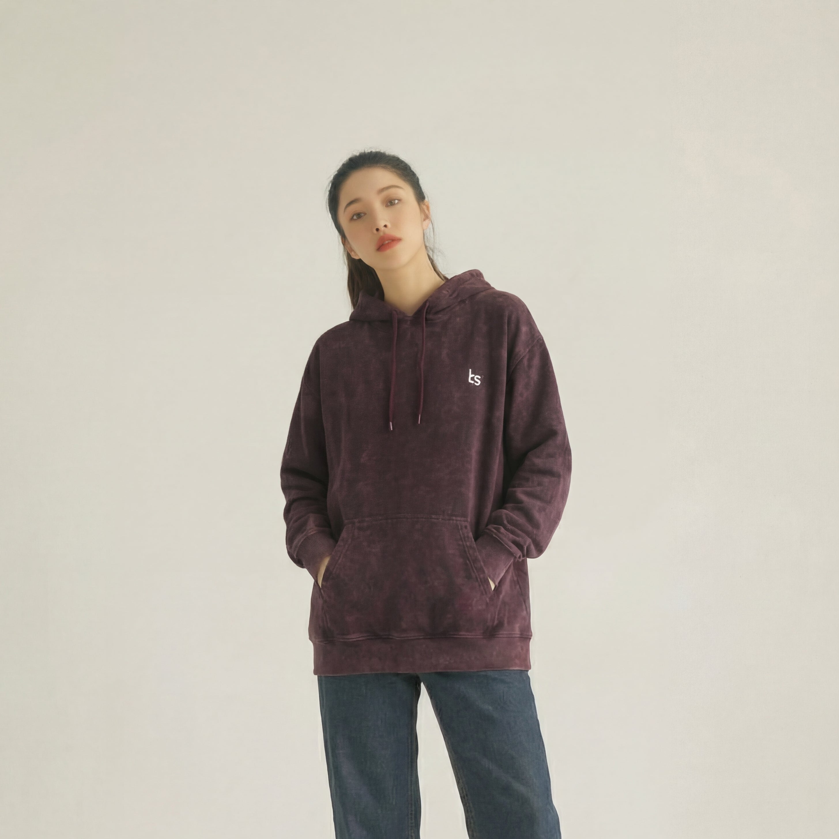 Person wearing a maroon hoodie and blue jeans on a beige background